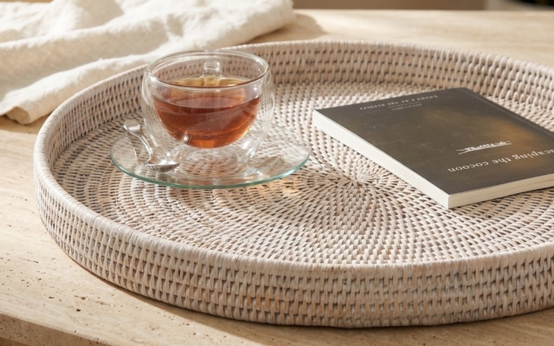 Round woven rattan serving tray resting on an ottoman